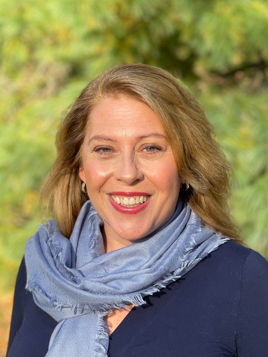 Denise Carreau, smiling, photographed outdoors against green foliage